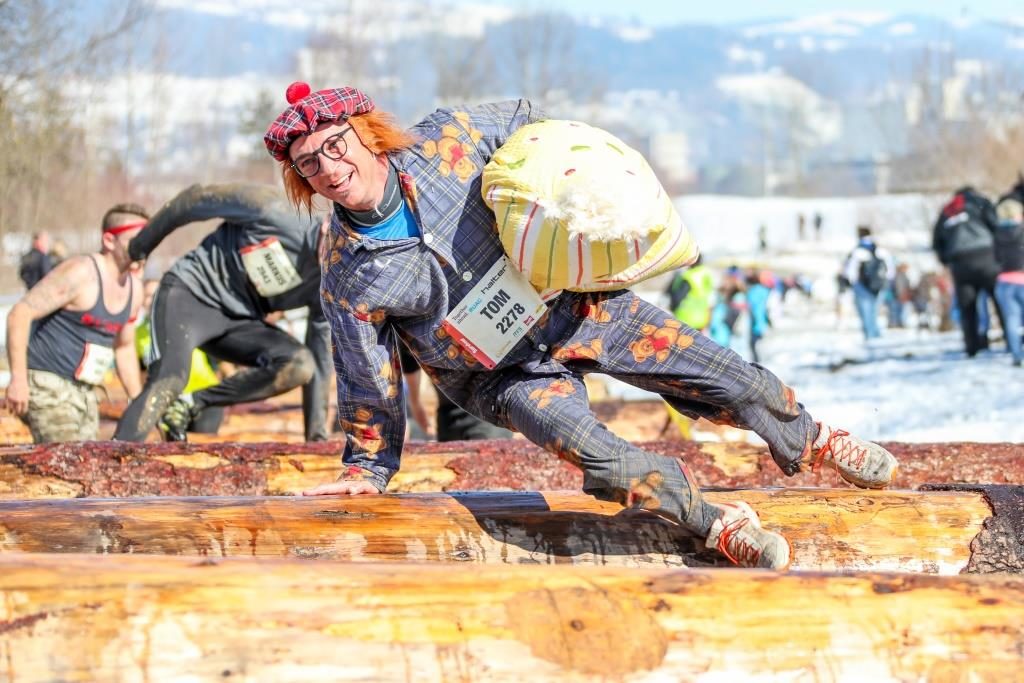 Ein Mann in ausgefallenem Kostüm (Schottenrock) springt beim Survivalrun in Thun auf dem Waffenplatz über einen Baustamm