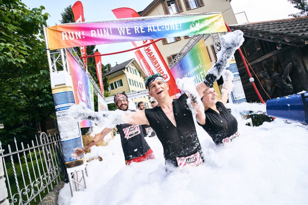 Drei Teilnehmende des StrongmanRun in Engelberg kämpfen sich durch das Schaumbad und breiten dazu jubelnd die Arme aus